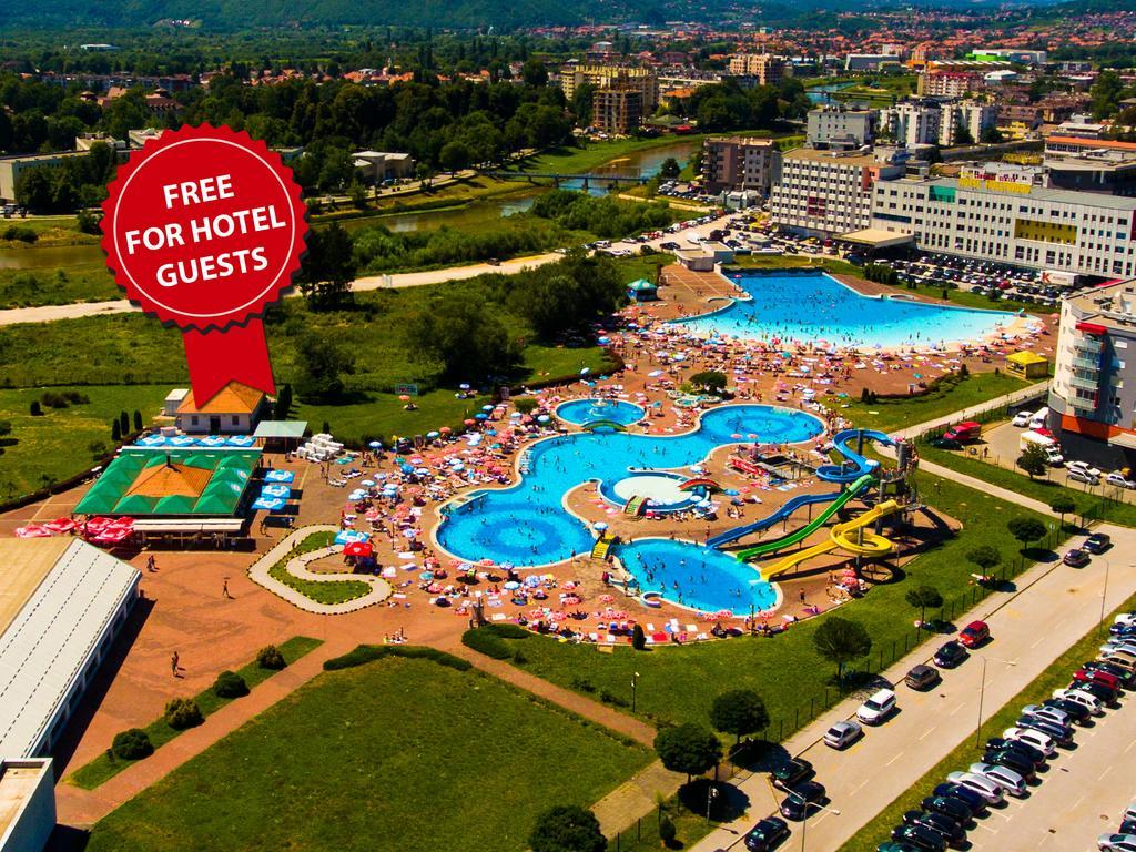 호텔 힐스 사라예보 콩그레스 앤 테르말 스파 리조트 Ilidža 외부 사진 The photo shows an aerial view of a large swimming pool area, likely part of a hotel or resort. There are several pools of different shapes and sizes, including one that resembles a Mickey Mouse shape. The area is filled with numerous sun loungers an